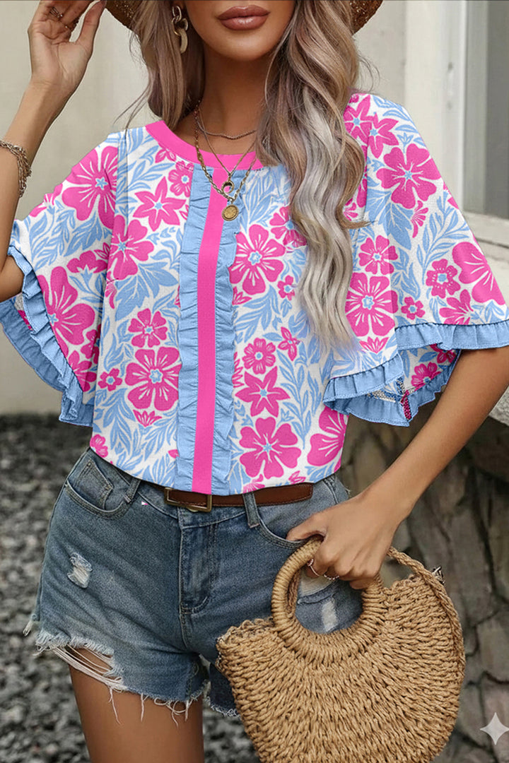 Woman wearing a floral blouse with ruffled sleeves and denim shorts, holding a straw bag.