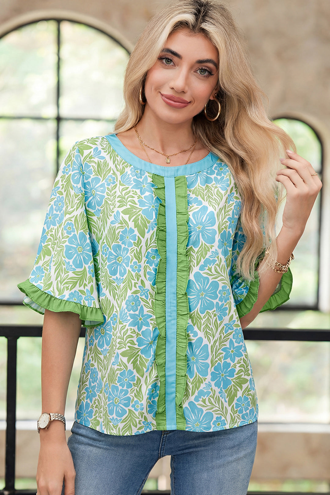 Woman wearing a floral blouse with green and blue pattern in front of a window.