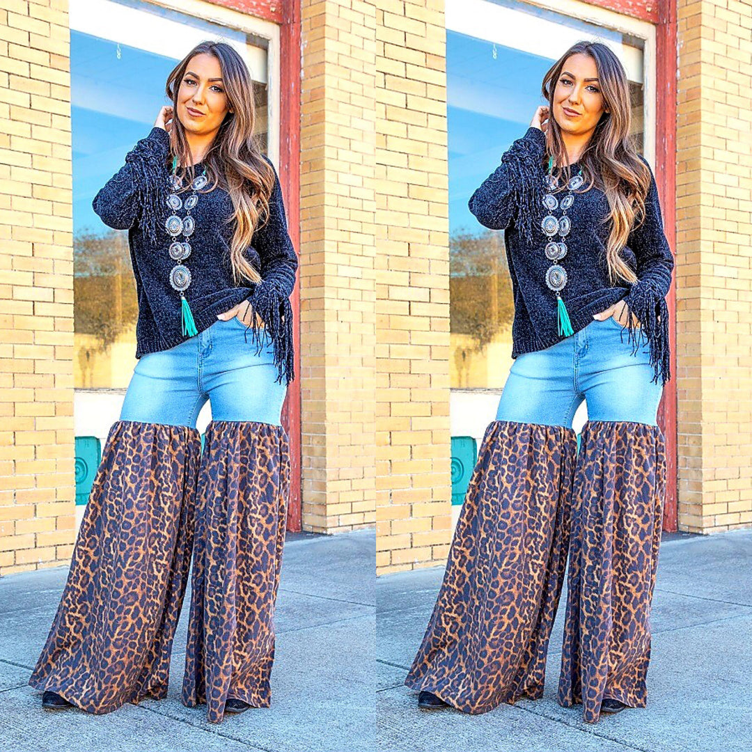 Woman wearing a dark blue cardigan with buttons, light blue jeans, and leopard print pants in front of a brick building.