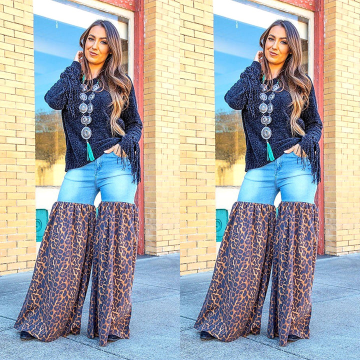 Woman wearing a dark blue cardigan with buttons, light blue jeans, and leopard print pants in front of a brick building.