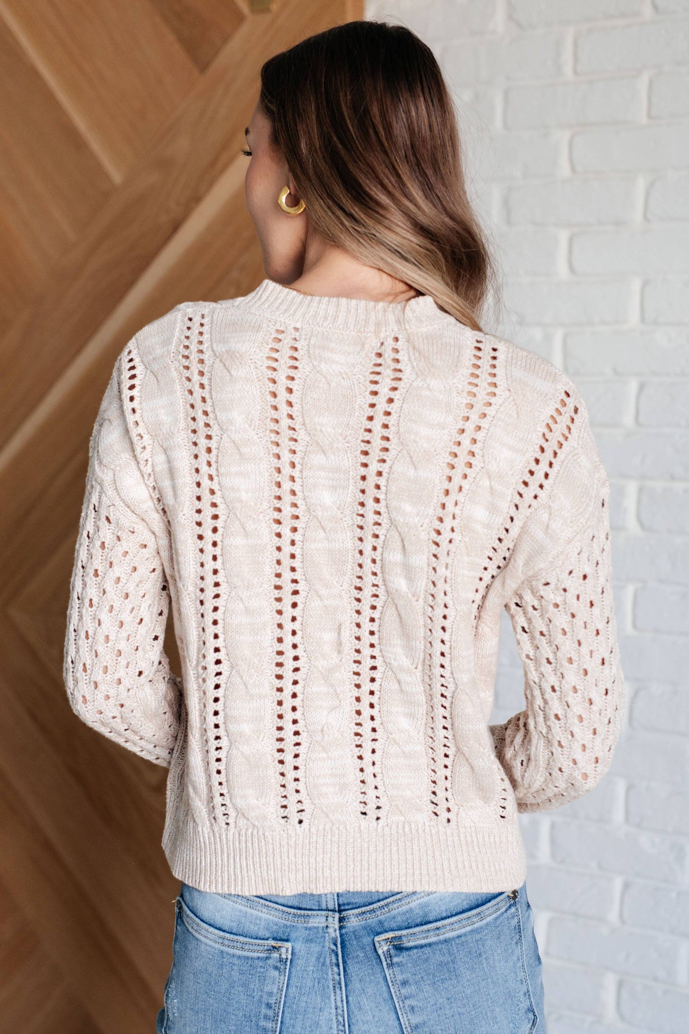 Back view of model in cable knit sweater and jeans.