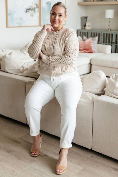 Plus-size model seated in ivory sweater and white pants.