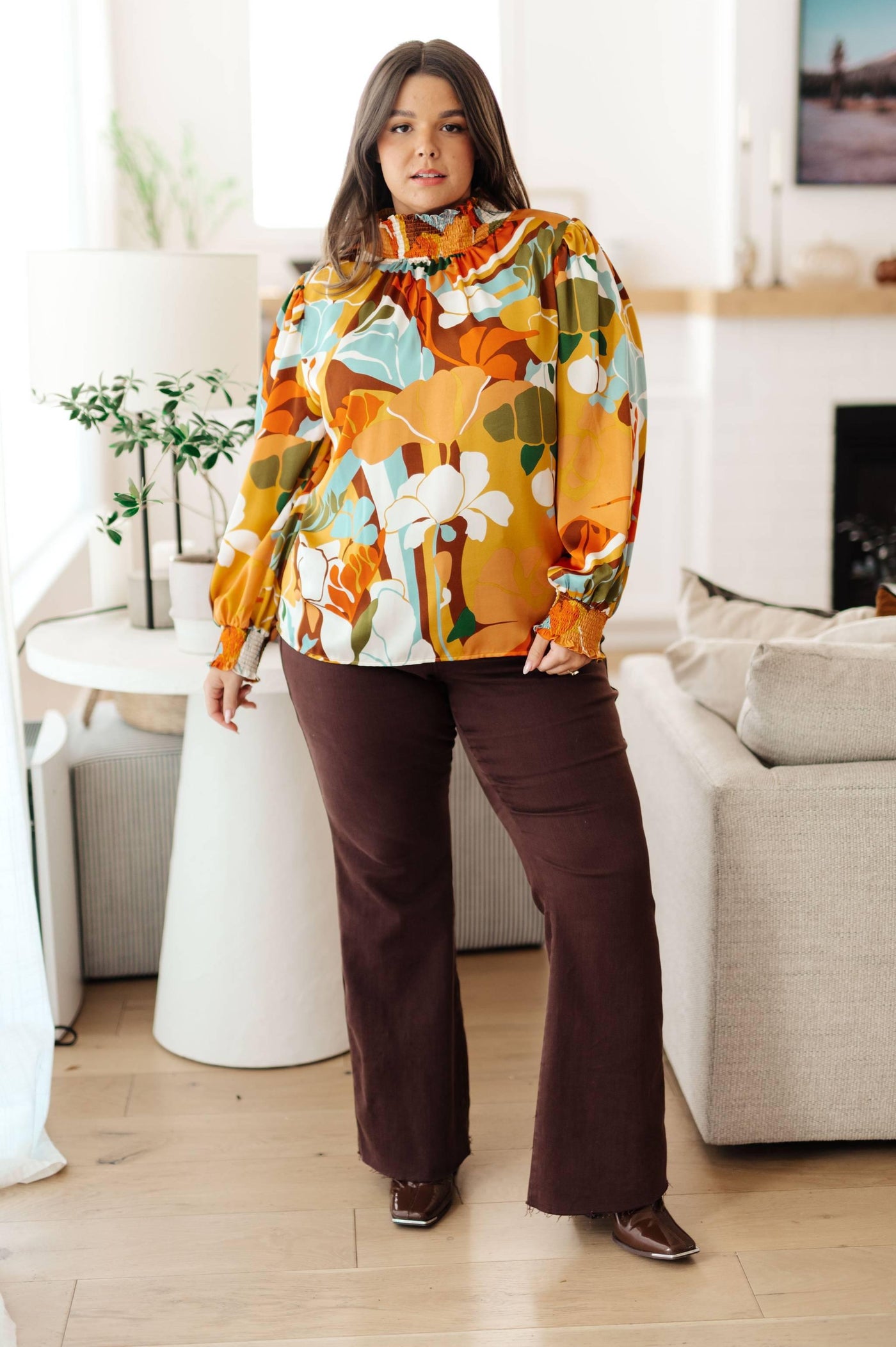 Model wearing floral mock neck blouse with brown pants.