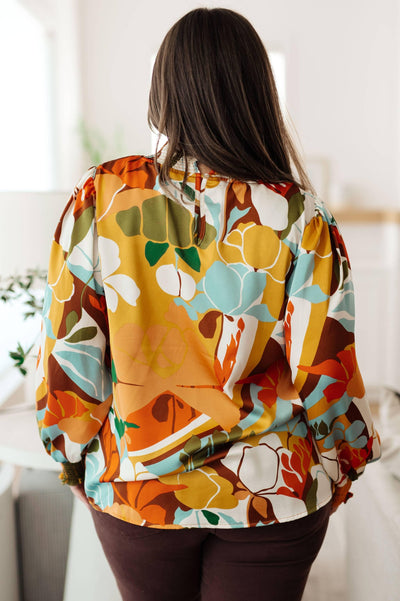 Back view of floral mock neck blouse, styled with dark pants.