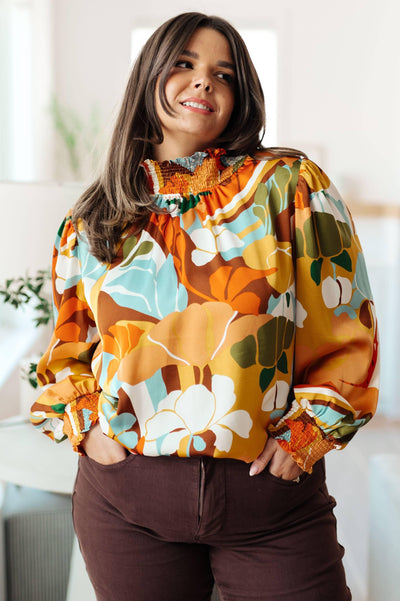 Bright floral blouse with mock neck, hands in pockets.