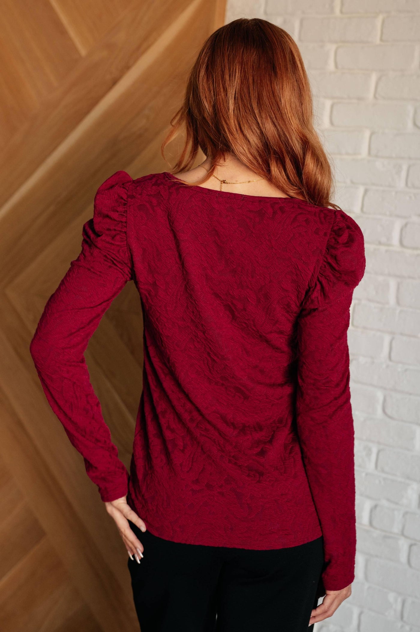 Back view of red ruched sleeve top, model indoors.