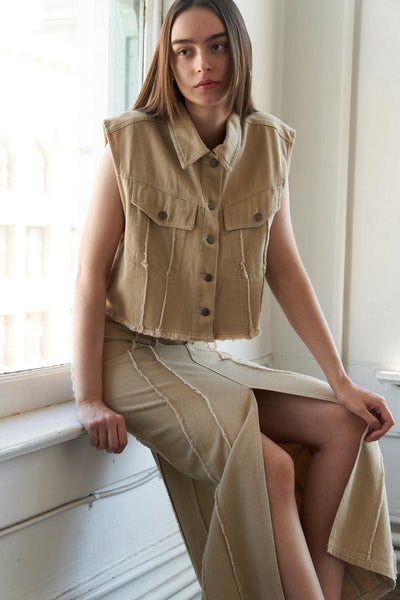 Model seated in taupe woven twill vest and skirt.