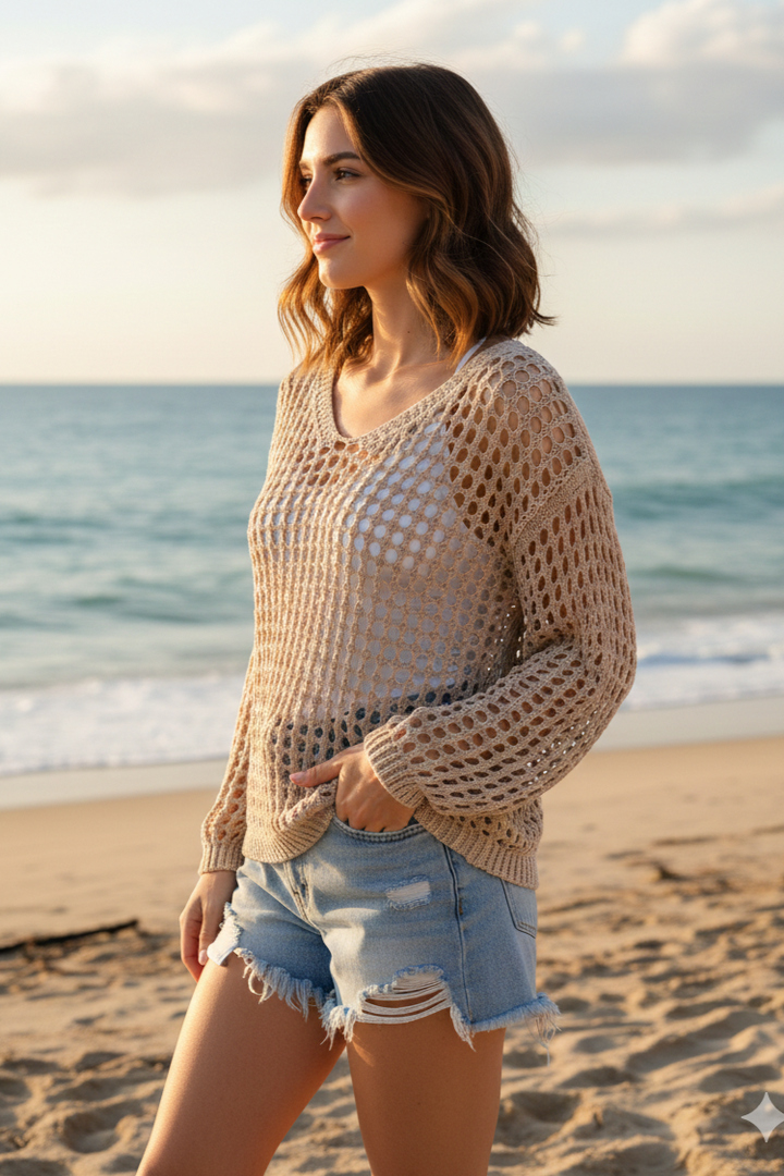Woman wearing a beige crochet sweater and denim shorts on a beach.