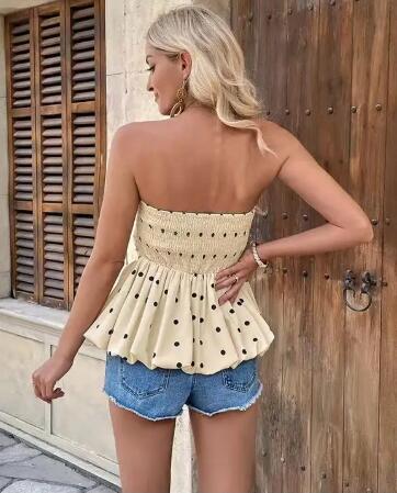 Woman wearing a polka dot top and denim shorts standing in front of a wooden door.
