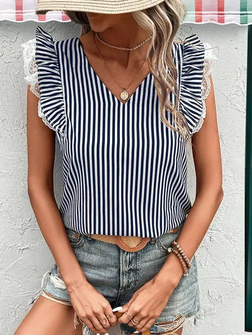 Woman wearing a black and white striped top with ruffled sleeves against a light gray wall.