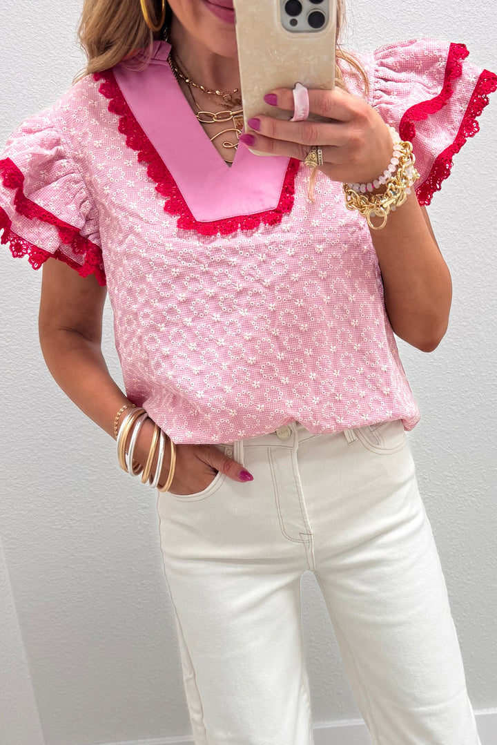 Person wearing a pink blouse with red trim and white pants, taking a mirror selfie.