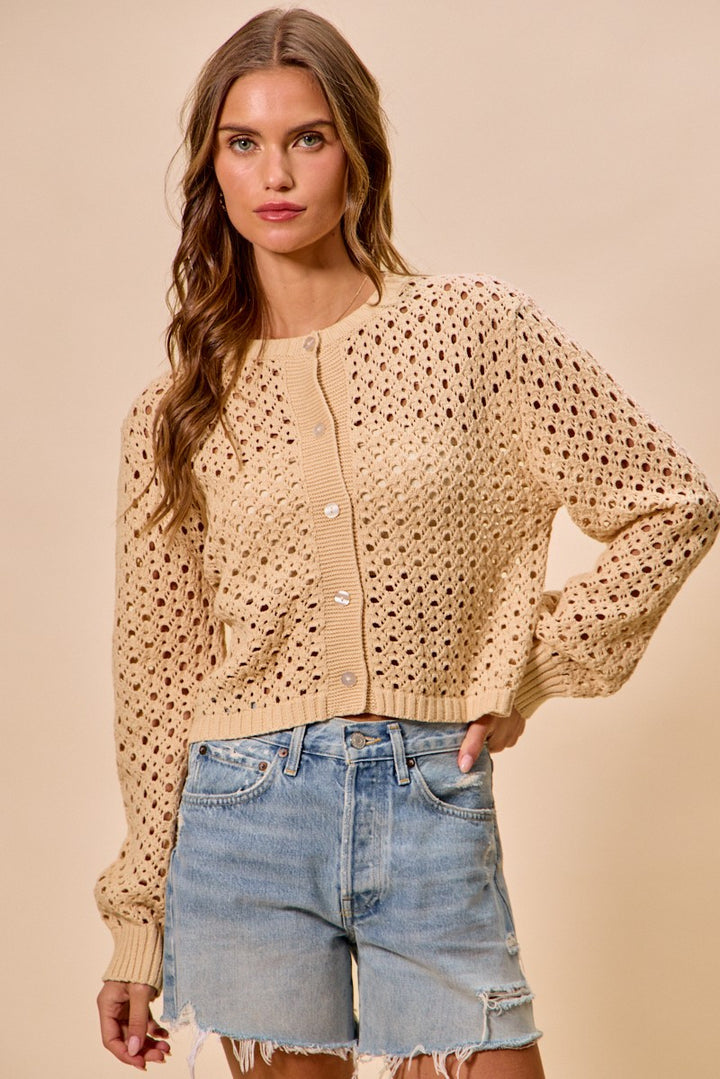 Woman wearing a beige knitted cardigan and denim shorts on a beige background