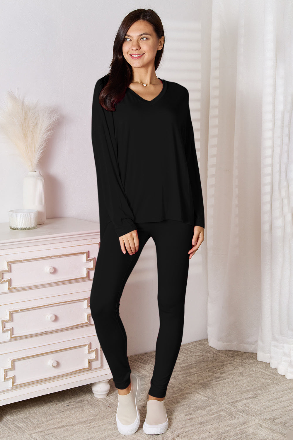 Woman wearing a black outfit standing in a room with white furniture and decor.