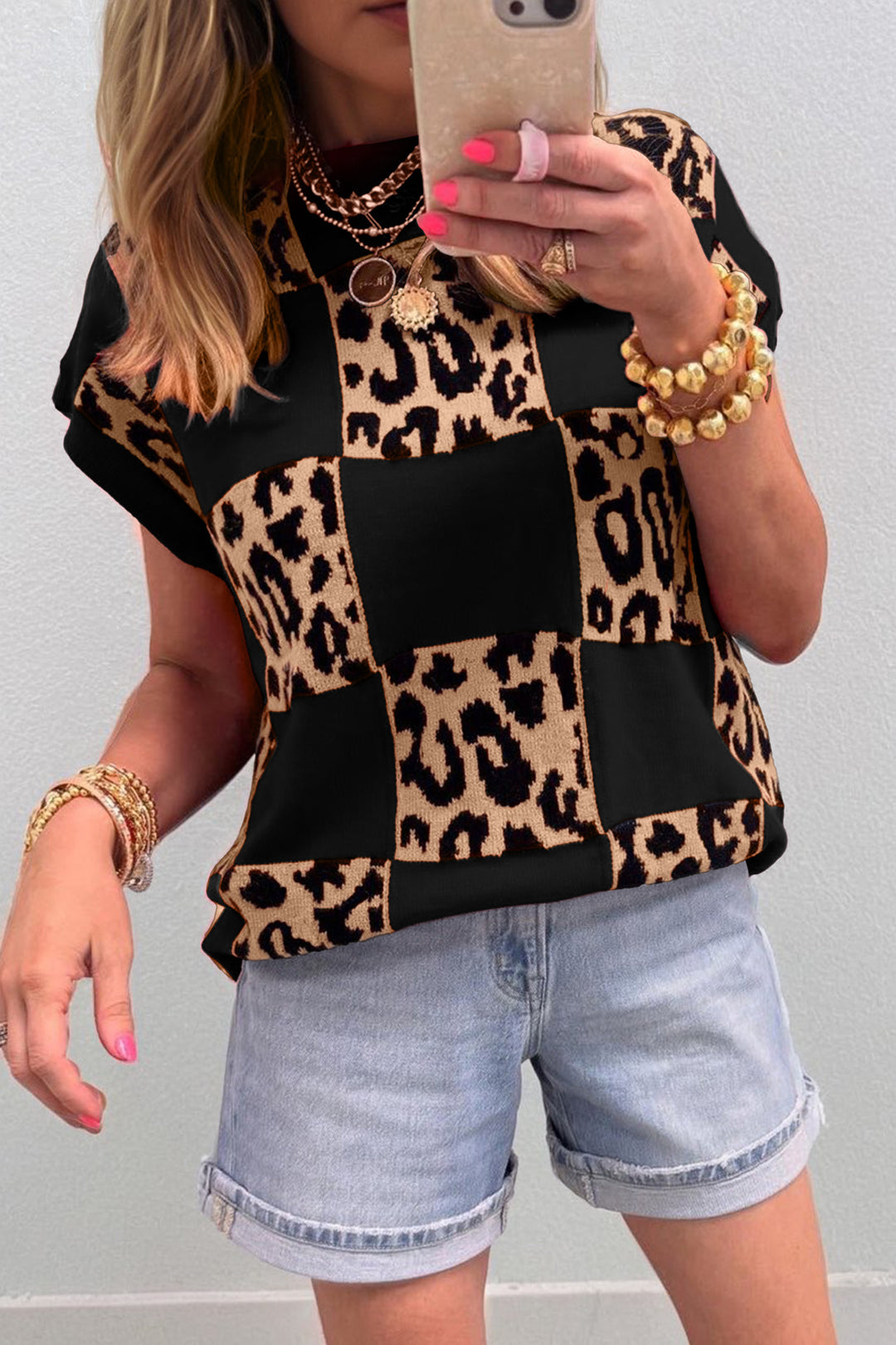 Person wearing a leopard print top and denim shorts, taking a selfie.